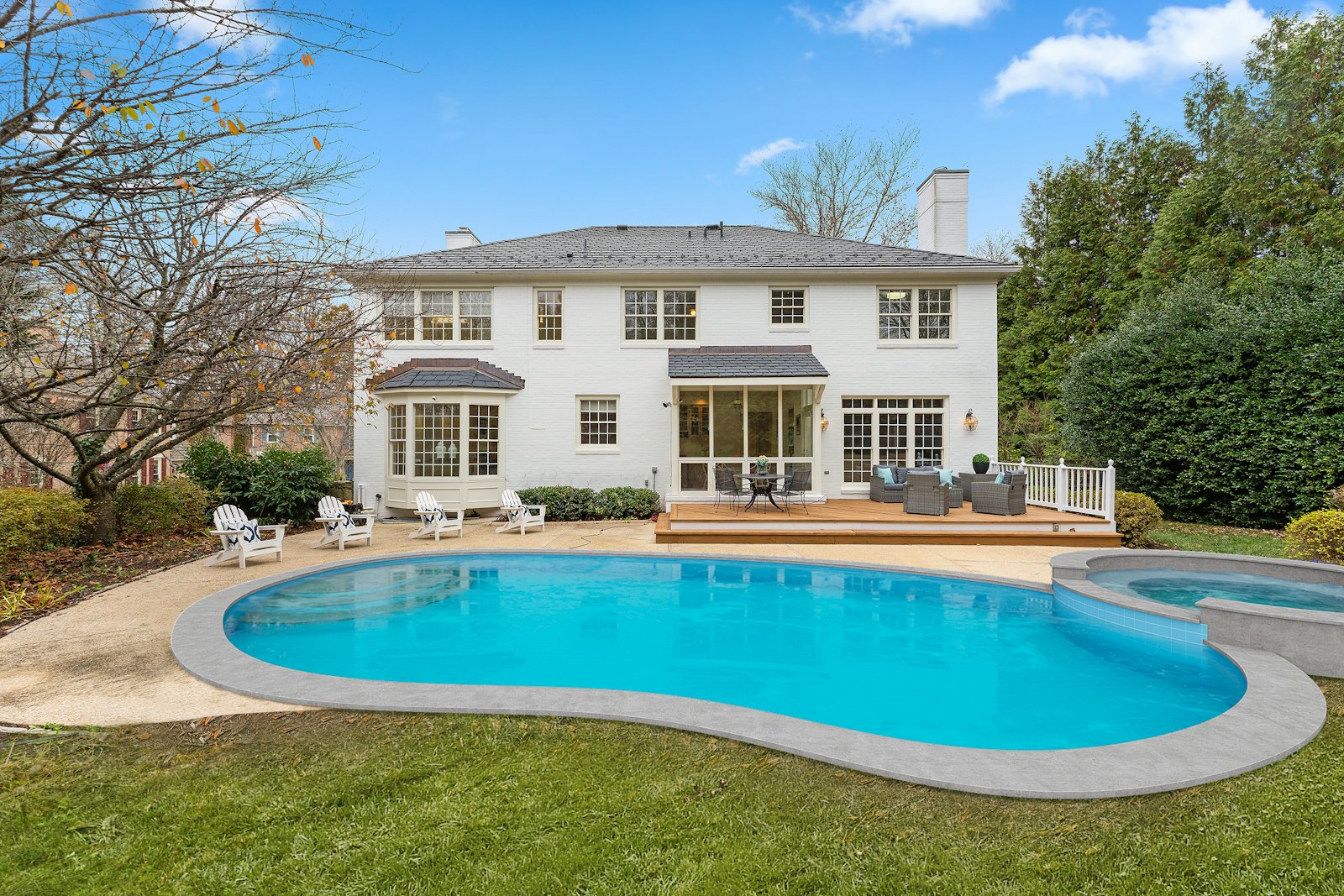 Backyard swimming pool and deck beside a white house