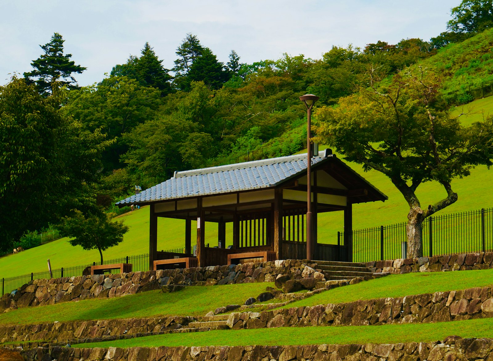 Wooden pavilion on a grassy hillside with stone retaining walls